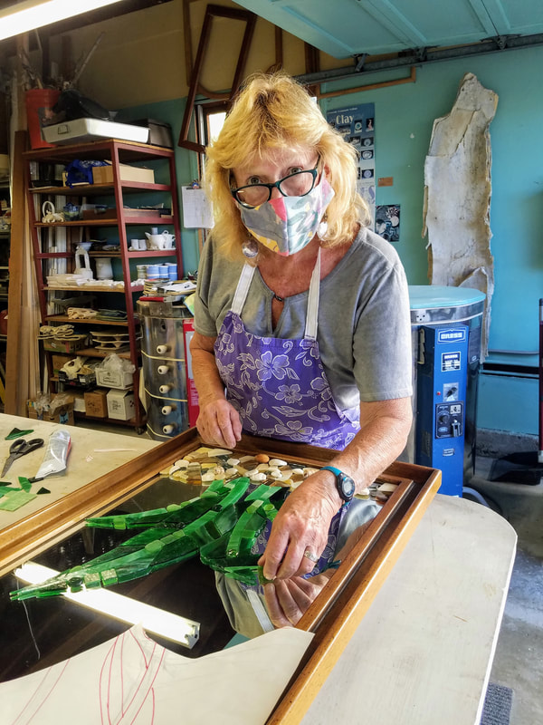 Kathryn in her garage studio space laying glass mosaic over a mirror.